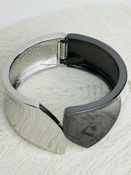 Silver and black tone cuff bracelet with sculptural leaf shape and polished finish on a textured white surface