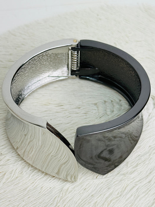 Silver and black tone cuff bracelet with sculptural leaf shape and polished finish on a textured white surface