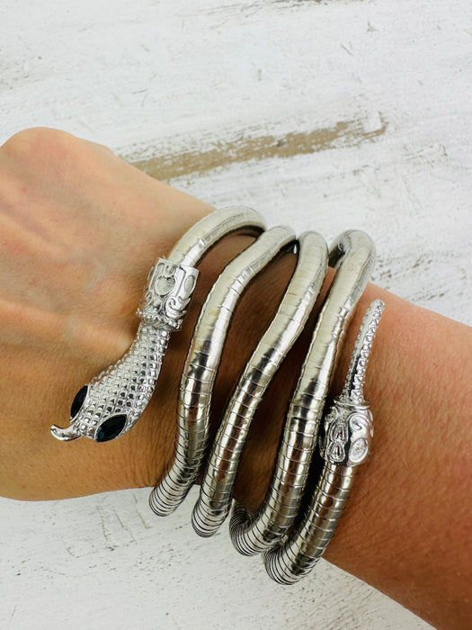 A silver-colored bracelet with a coiled design and decorative elements, displayed on a person's wrist.