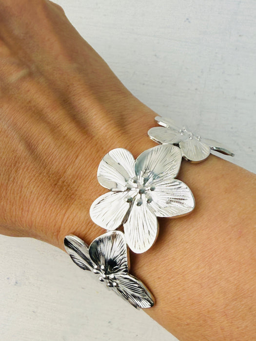 A silver cuff bracelet with blooming floral details, displayed on a model