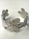 A silver cuff bracelet with blooming floral details, displayed against a white background.