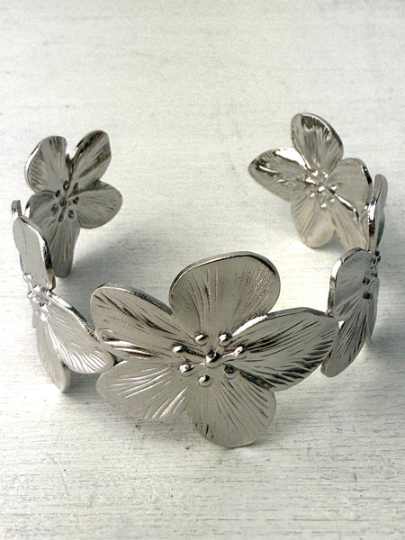 A silver cuff bracelet with blooming floral details, displayed against a white background.