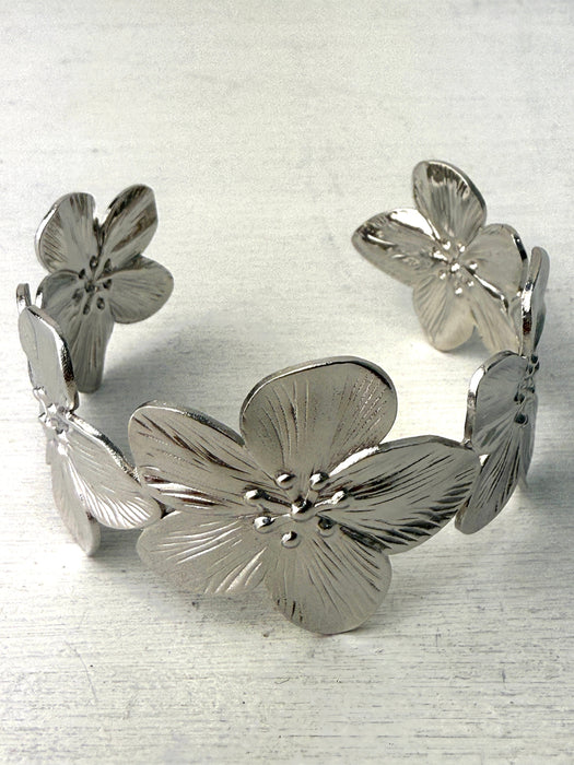 A silver cuff bracelet with blooming floral details, displayed against a white background.