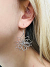 A close-up of a silver floral dangle earring.