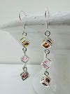 close up of earrings featuring triple crystal caged cubes with yellow, pink and purple crystal detail, displayed against a light background.