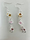 close-up of earrings featuring triple crystal caged cubes with yellow, pink and purple crystal detail.