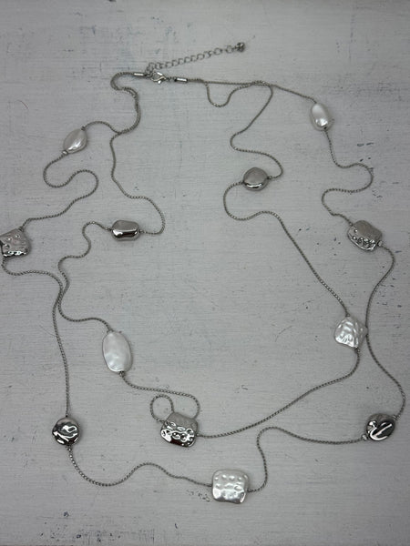 Long silver necklace with textured geometric charms displayed on mannequin