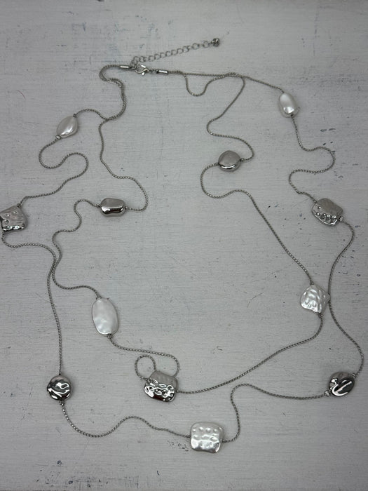Long silver necklace with textured geometric charms displayed on mannequin