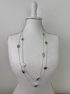 Long silver necklace with textured geometric charms displayed on mannequin