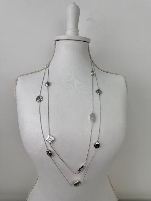 Long silver necklace with textured geometric charms displayed on mannequin