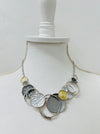 A necklace with a silver and gold color scheme, featuring a series of circular pendants in different shades and a chain, displayed on a mannequin.