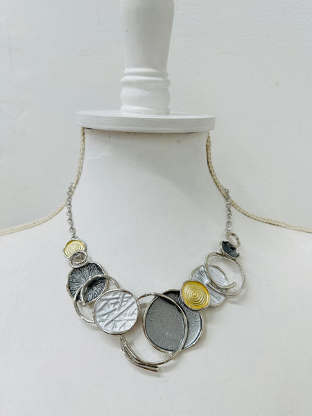 A necklace with a silver and gold color scheme, featuring a series of circular pendants in different shades and a chain, displayed on a mannequin.