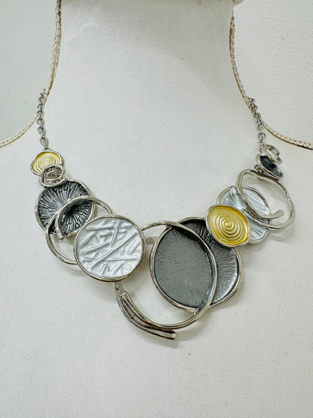 A necklace with a silver and gold color scheme, featuring a series of circular pendants in different shades and a chain displayed on a mannequin.