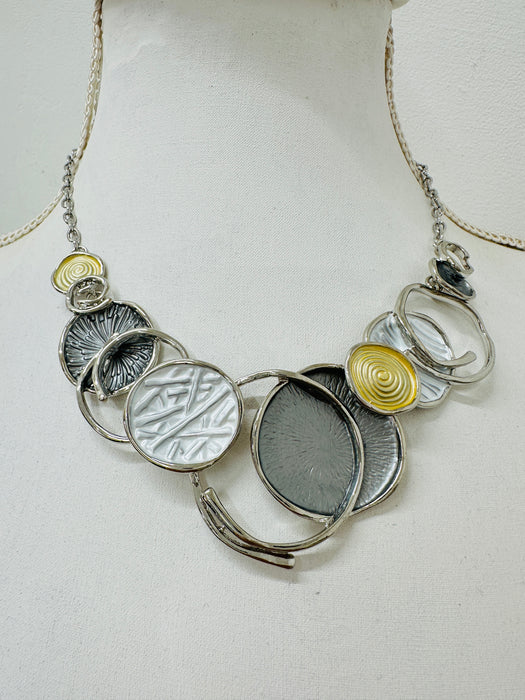 A necklace with a silver and gold color scheme, featuring a series of circular pendants in different shades and a chain displayed on a mannequin.