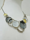 A necklace with a silver and gold color scheme, featuring a series of circular pendants in different shades and a chain displayed on a mannequin.