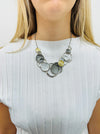 A necklace with a silver and gold color scheme, featuring a series of circular pendants in different shades and a chain displayed on a model.