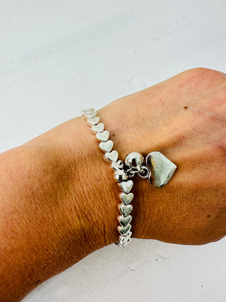 Silver heart-shaped bracelet on a wrist against a light background