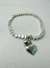 A silver bracelet with a heart-shaped charm, displayed against a white background.