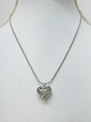 A silver-colored necklace with a heart-shaped pendant on a mannequin.