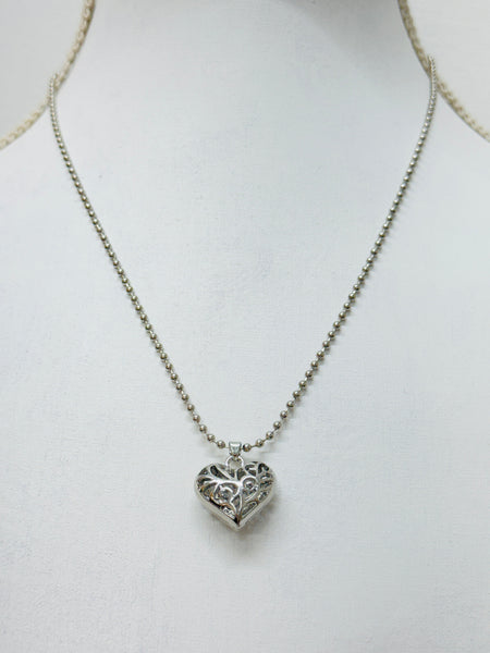 A silver-colored necklace with a heart-shaped pendant on a mannequin.