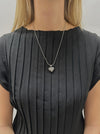 Person wearing a black pleated dress with a necklace featuring a heart-shaped pendant.