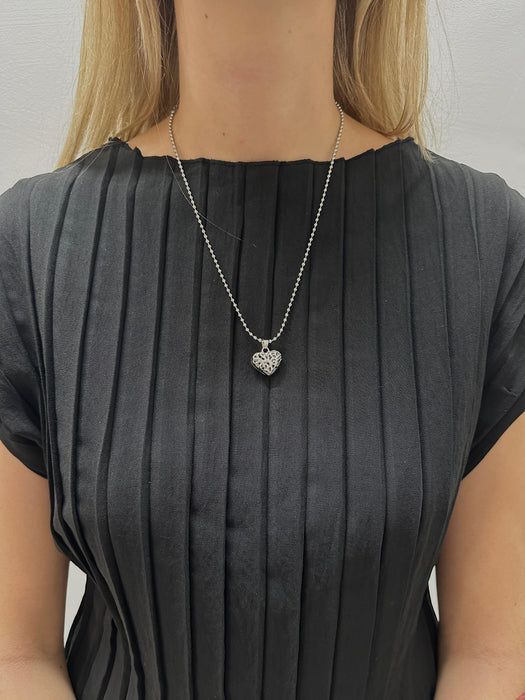 Person wearing a black pleated dress with a necklace featuring a heart-shaped pendant.