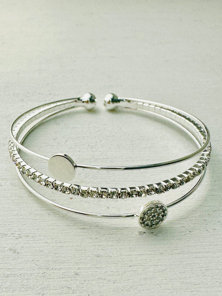 A silver-plated cuff bracelet with a decorative crystal element in the center, presented against a light background.