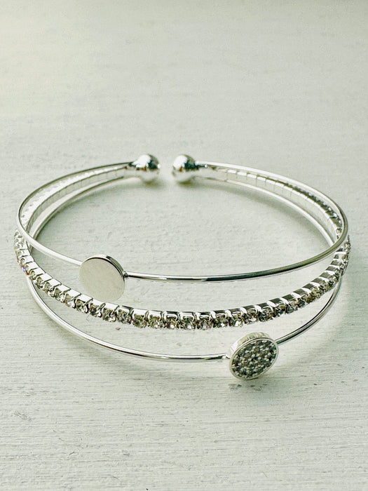 A silver-plated cuff bracelet with a decorative crystal element in the center, presented against a light background.