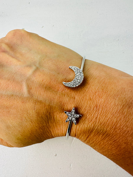A silver bracelet with a crescent moon and star design worn on a person's wrist.
