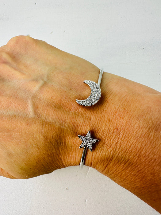 A silver bracelet with a crescent moon and star design worn on a person's wrist.