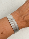 A close-up of a person's wrist wearing a multi-strand silver snake chain bracelet against a light textured background.