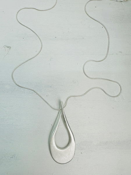 A silver necklace with a teardrop-shaped pendant on a light background.
