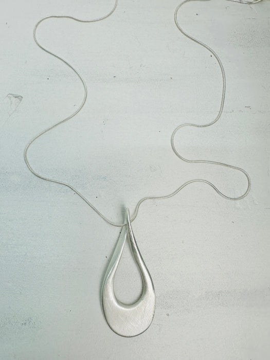 A silver necklace with a teardrop-shaped pendant on a light background.