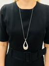 silver-tone necklace with a long chain and a teardrop-shaped metal pendant, displayed on a model