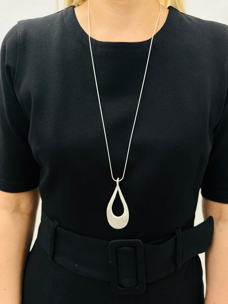 silver-tone necklace with a long chain and a teardrop-shaped metal pendant, displayed on a model