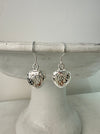 A pair of silver dangle earrings with openwork heart charms displayed on a white stand.