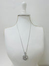 A silver-colored necklace with a long chain and a flower-style pendant, displayed on a mannequin bust.