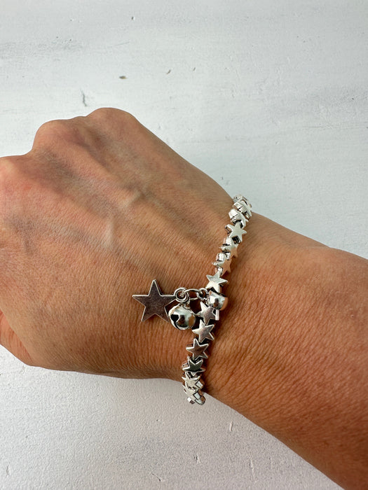 Silver bracelet with star charms on a wrist against a light background