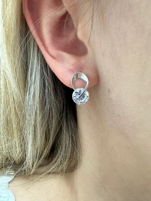 A close-up image of a person wearing a silver stud earring with a crystal detail.