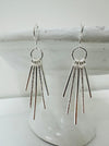 A pair of silver-colored earrings with a geometric design, featuring multiple dangling lines from a central circle.