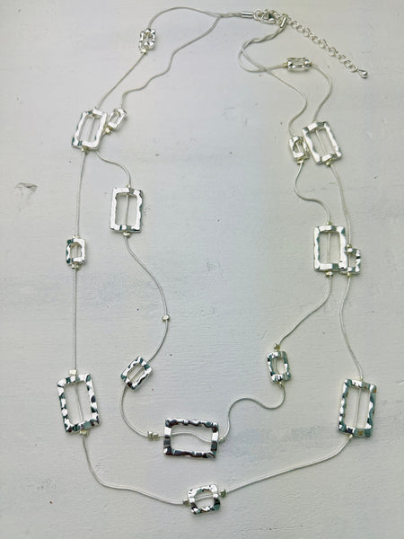 A silver necklace with multiple geometric pendants laid out on a flat surface.