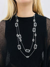 A person wearing a black top and a silver-colored necklace with geometric shapes.