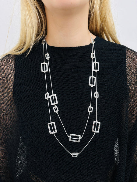 A person wearing a black top and a silver-colored necklace with geometric shapes.
