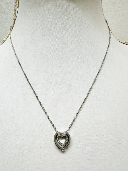 A silver necklace with a double heart pendant featuring a crystal detail, displayed on a mannequin.