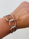 Modern silver-tone cuff bracelet with open link design, displayed on a model.