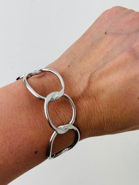 Modern silver-tone cuff bracelet with open link design, displayed on a model.