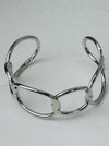 Modern silver-tone cuff bracelet with open link design, displayed on a table.