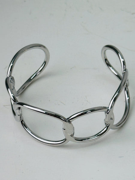 Modern silver-tone cuff bracelet with open link design, displayed on a table.