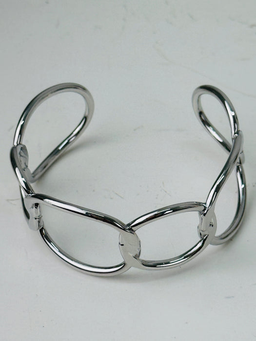 Modern silver-tone cuff bracelet with open link design, displayed on a table.