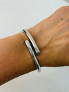A sleek silver bracelet with a modern open-ended design, displayed on a model.